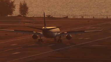 Günbatımında yolcu uçağı silueti, deniz arka planı. Uçak geliyor, fren yapıyor, flaplar kalkıyor.