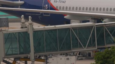 PHUKET, THAILAND - 25 Şubat 2023: Teleskopik iskele havaalanı. Pistteki uçağa yol açın. Yolcuların siluetleri teleskopik bir iskelede koridordan geçiyor.