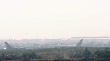 BANGKOK, THAILAND - 21 HAZİRAN 2023: Tayland Havayolları 'nın geniş gövdeli Boeing 777' si Suvarnabhumi Havaalanı 'ndan kalkmadan önce hızlanıyor. Puslu ve arka planda bir uçak