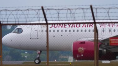 PHUKET, THAILAND - 28 HAZİRAN 2023: Juneyao Havayolları 'nın Airbus A320' si Phuket Havaalanında taksicilik yapıyor. Çin Havayolları. Yolcu uçağı havaalanında, çitin ötesini görüyor. Turizm seyahati kavramı
