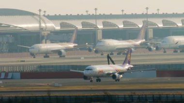 BANGKOK, THAILAND - 21 HAZİRAN 2023: Yolcu uçağı Airbus A320, Tayland 'dan HS-TXF Suvarnabhumi Havaalanı' ndaki piste iniyor. Havaalanı. Terminalde sıra sıra uçaklar, arka plan