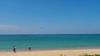 Mavi denizin üzerinden inmek için yaklaşan bir uçak. İnsanlar sahilde bir uçağın fotoğrafını çekiyor. Turizm ve seyahat kavramı