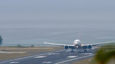 PHUKET, THAILAND - Şubat 03, 2023: Boeing 777, RA-73272 Pegas Fly uçağı Phuket havaalanına indikten sonra fren yapıyor. Geniş gövdeli varış. Flaplar yukarı, hız aşağı. Uçak ve deniz arka planı