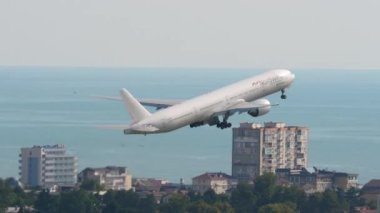 SOCHI, RUSSIA - 02 AĞUSTOS 2022: Boeing 777, Nordwind Havayolları 'ndan RA-73847 Sochi havaalanından havalanıyor, yan görüş. Uçak kalkıyor. Uçak şehir ve denizin üzerinden tırmanıyor. İniş takımlarını kaldır