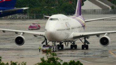 PHUKET, THAILAND - 02 Aralık 2016: Tayland Havayolları 'nın Boeing 747 sefer sayılı yolcu uçağı, Phuket Havaalanı, ön görüş. Traktör jumbo jeti çekiyor. Havaalanı ve yağmur. Turizm ve seyahat kavramı