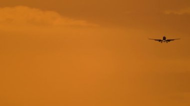 Parlak günbatımı gökyüzünde bir jet uçağı inişe yaklaşıyor. Arka planda, tanınmayan bir uçağın silueti. Sineklerin sinematik çekimi, güzel gün batımı.
