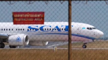 PHUKET, THAILAND - 22 Şubat 2023: Boeing 737 MAX 9, Scat Airlines 'ın UP-B3727' si Phuket havaalanında taksicilik yapıyor. Havaalanı çitlerinin arkasındaki yolcu uçağının orta boy görüntüsü. Seyahat kavramı