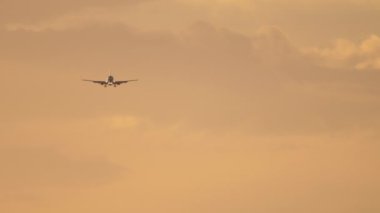 Parlak günbatımı gökyüzünde bir jet uçağı inişe yaklaşıyor. Arka planda, tanınmayan bir uçağın silueti. Sineklerin sinematik çekimi, güzel gün batımı.