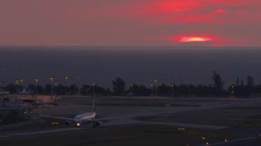 Taksiyoldaki bir jet uçağının sinematik görüntüleri. Günbatımı aydınlatma havaalanı. Yuvarlak kırmızı güneş ufukta batar