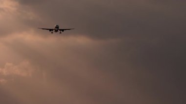 Jet uçağı gün batımında uçar. Uçak geliyor. Bulutlu alacakaranlık gökyüzüne inmeden önce bir uçak yaklaşıyor.