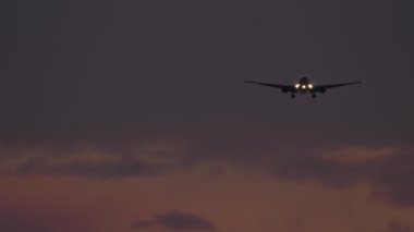 Jet uçağı inişe geçiyor, gece gökyüzünde siluet var. Uçak iniyor. Uçak farları açık uçuyor. Uçak alacakaranlıkta uçar.