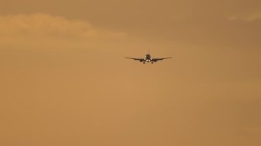 Jet uçağı inişe geçiyor. Arka planda gökyüzünde siluet uçak var. Sineklerin sinematik çekimi, güzel gün batımı.