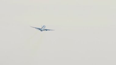 Commercial passenger airliner climbing after takeoff in the blue sky. Rear view long shot, plane turning