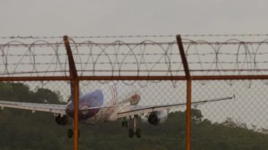 PHUKET, THAILAND - 16 Şubat 2023: Tay Gülüşü 'nün jet uçağı gün batımında uçar. Uçak geliyor. Bulutlu alacakaranlık gökyüzüne uçak iniyor. İniş yaptı, pistte fren yapıyor. Flaplar yukarı. Havaalanı çiti