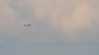 Jet plane approaching landing at sunset. Cinematic footage of a commercial aircraft flies against the background of illuminated clouds.