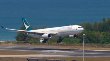 PHUKET, THAILAND - 20 Şubat 2023: Airbus A330 Cathay Pacific iniş ve frenleme, yan görüş. Uçak mavi denizin üzerinde uçar. Uçak geliyor. Seyahat havacılık kavramı