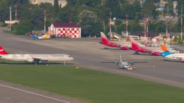 SOCHI, Rusya - 29 Temmuz 2022: panoramik havaalanı manzarası. Adler Havaalanı, Sochi 'deki UTAir' in ATR-72 uçağını römorkör çekiyor. Uçak sırası park edilmiş, kenetlenmiş. Nordwind pistte taksicilik yapıyor. Seyahat