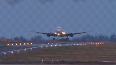 Bir jet uçağının iniş yaptığı, piste dokunduğu ve frenlediği sinematik görüntüler. Uçak geldi. Çitin arkasından bak. Pist aydınlatması. Turizm ve seyahat kavramı