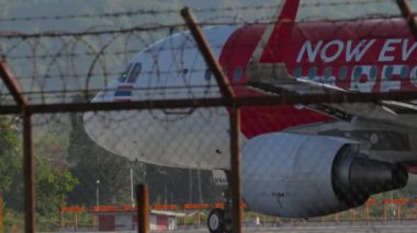 PHUKET, THAILAND - 10 Şubat 2023: Airbus A320 from AirAsia with Now Everybody Can Fly Livery taxiating to the poway at Phuket havaalanı. Havaalanı çitlerinin dışındaki uçak.