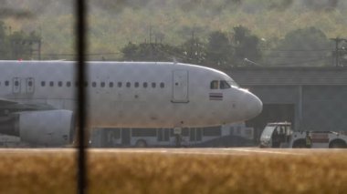PHUKET, THAILAND - 19 Şubat 2023: Phuket Havaalanında Tayland Jet 'in Airbus A320 uçağını çeken traktör, yan görüş. Havaalanındaki uçak. Turizm ve seyahat kavramı.