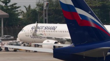 PHUKET, THAILAND - 25 Şubat 2023: Phuket havaalanında Qanot Sharq 'ın Airbus A321' ini çeken traktör. Aeroflot uçak kuyruğu ön planda. Yolcu uçağı kalkışa hazır.