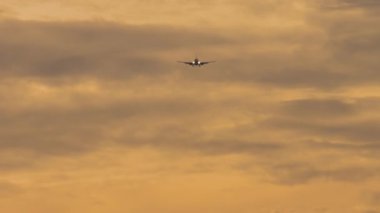 Jet uçağı inişe geçiyor. Yolcu uçağı gün batımında gökyüzünde uçuyor, ön görüş, uzak çekim