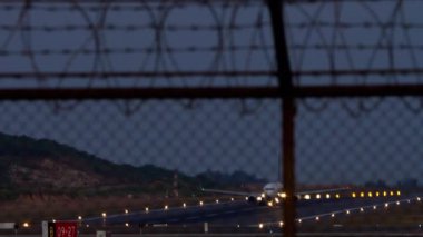 Ticari jet uçağı gece kalkıyor. Havaalanı çitlerinden bak. İniş ışıkları pisti aydınlatıyor
