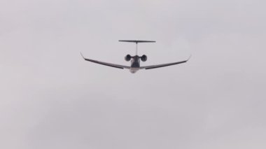 Tanımlanamayan bir üniforması olan küçük bir jet yolcu uçağı arka planda uçuyor.