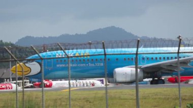 PHUKET, THAILAND - 27 Kasım 2015: Video Boeing 737, Nok Air 'in HS-DBD' si Phuket havaalanında pist üzerinde taksicilik yapıyor. Havaalanı çitlerinin arkasında bir uçak var. Havaalanı