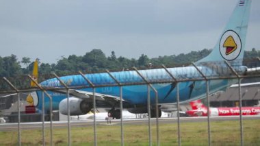 PHUKET, THAILAND - 27 Kasım 2015: Sinematik çekim, Nok Air 'in Boeing 737' si Phuket Havaalanı pistinde yan görüş. Havaalanı çitlerinin arkasında Asya uçağı var. Havaalanı