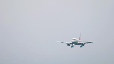İniş için yaklaşan bir yolcu uçağının ön görüntüsü. Gri gökyüzünde bir uçak