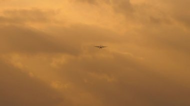 Unrecognizable jet plane silhouette approaching to land in sunset golden sky. Tourism and travel concept