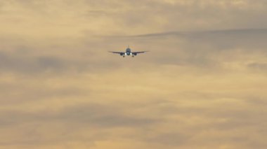 Jet uçağı inişe geçiyor, gün batımında gökyüzüne iniyor. Gökyüzünde uçan bir uçağın ön görüntüsü. Turizm ve seyahat konsepti. Uçak geliyor.