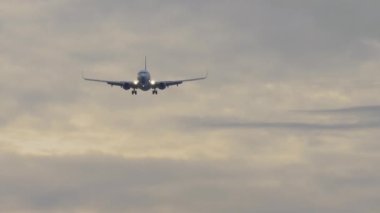 İniş yapan bir jet uçağının yavaş çekim görüntüleri. Yolcu uçağı gün batımında gökyüzünde uçuyor, ön görüş, uzak çekim