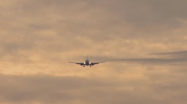 İniş yapan bir jet uçağının görüntüsü. Yolcu uçağı gün batımında gökyüzünde uçuyor, ön görüş, uzak çekim