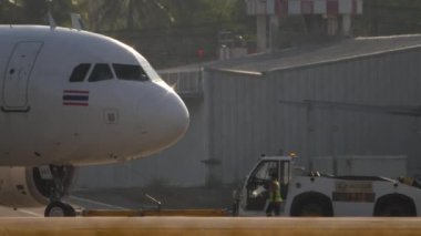 PHUKET, THAILAND - 19 Şubat 2023: Airbus A320, Phuket Havaalanı 'ndaki Tayland Jet HS-VKT, yan görüş. Arka planda güneş ışığı alan bir uçak. Traktör uçağı çekiyor. Turizm ve seyahat kavramı.
