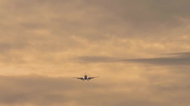 İniş yapan bir jet uçağının görüntüsü. Yolcu uçağı gün batımında gökyüzünde uçuyor, ön görüş, uzak çekim