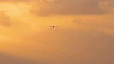 İniş yapan bir jet uçağının görüntüsü. Yolcu uçağı gün batımında gökyüzünde uçuyor, ön görüş, uzak çekim