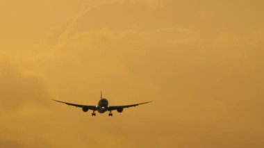 Jet airplane approaching to land in the sunset sky, long shot static. Tourism and travel concept