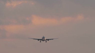 Tanımlanamayan bir üniforması olan bir jet uçağı pembe gün batımına iniyor.