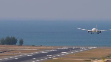 Geniş gövdeli uçak adaya iniyor. Yolcu tahtası geliyor. Mavi deniz arka planı.