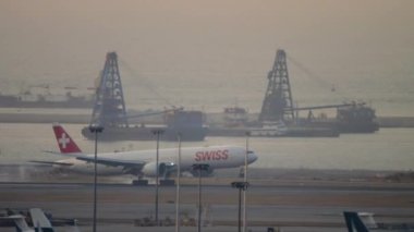 HONG KONG - 07, 2019: Boeing 777 SWISS inişi, Hong Kong havaalanında gün batımında dokunmak ve fren yapmak, uzak görüş. SWISS İsviçre 'nin en büyük havayolu şirketidir.