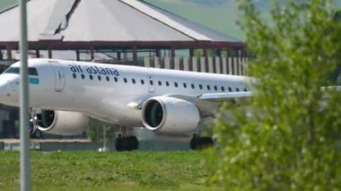 ALMATY, KAZAKHSTAN - 5 Mayıs 2019: yan görüş, Embraer E190 yolcu uçağı, Air Astana P4-KHB Almaty havaalanındaki piste iniyor. İnişten sonra uçuş frenleri. Spoiler hazır.