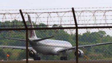 PHUKET, THAILAND - 26 HAZİRAN 2023: Airbus A330-302, Katar Havayolları 'nın A7-AEO' su Phuket havaalanından kalkışa hazırlanıyor. Havaalanı çitlerinin arkasında, dikiz aynasından, orta mesafeden.