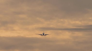 Jet uçağı inişe geçiyor. Yolcu uçağı bulutlu günbatımı gökyüzünde uçar, ön görüş, uzak çekim. Havacılığın sinematik görüntüleri. Arkaplan kıpkırmızı gökyüzü