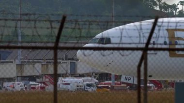 PHUKET, THAILAND - 25 Ocak 2023: Emirates 'ten Boeing 777 sefer sayılı yolcu uçağı Phuket Havaalanı, yan görüş. Havaalanı çitlerinin dışında kocaman geniş gövdeli bir uçak. Seyahat kavramı