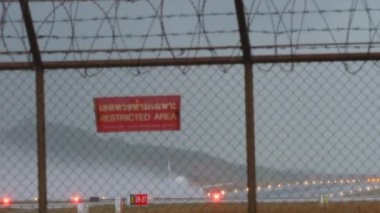 Uçak, Phuket Havaalanı 'ndan havalanmadan önce hızlanıyor. Islak bir pistte su püskürterek hızlanan uçak. Çitin arkasından bak. Kırmızı İşaret Yasak Bölge
