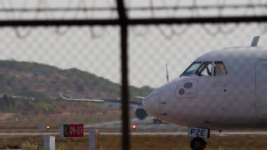 PHUKET, THAILAND - 19 Şubat 2023: Yolcu uçağı ATR 72-600, HS-PZE Bangkok Havayolları kalkış için Phuket havaalanı, yan görüş, havaalanı çitleri üzerinden pist