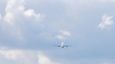 Mavi bulutlu gökyüzünde bir uçak. Jet uçağı kalkıyor, kalkıyor, dikiz manzaralı. Yüksekliğe tırmanan uçağın silueti.
