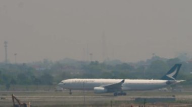 BANGKOK, THAILAND - 01 Mart 2023: Yolcu uçağı Airbus A330 Cathay Pacific, Suvarnabhumi Havaalanı, yan görüş. Hava sahasında sis.